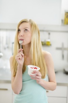 Thoughtful teenager girl eating yogurt in kitchen